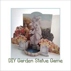 May include: A DIY garden statue game with a pop-up scene featuring a white statue of a woman in a garden setting with flowers and a small pond. The text "DIY Garden Statue Game" is printed below the scene.