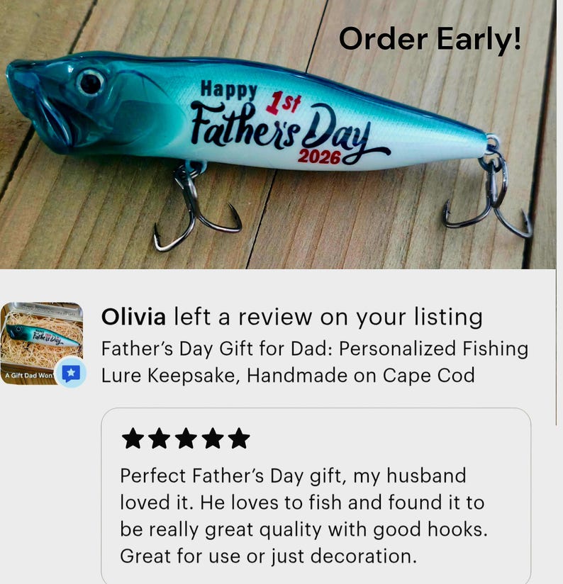 May include: A blue and white fishing lure with a gradient finish, featuring the black text "Happy 1st Father's Day 2026" printed on the side. The lure includes two metal treble hooks attached to the bottom and a realistic eye near the front.