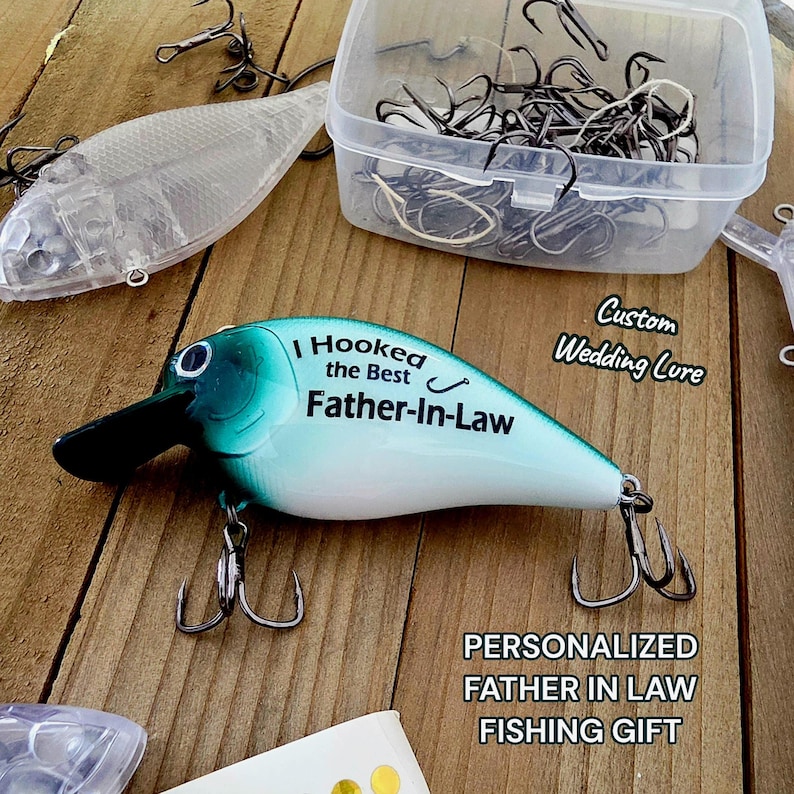 a fishing lure with a personalized message, a clear plastic container filled with fishing hooks, and a wooden surface with a sign that reads "Custom Wedding Lure".