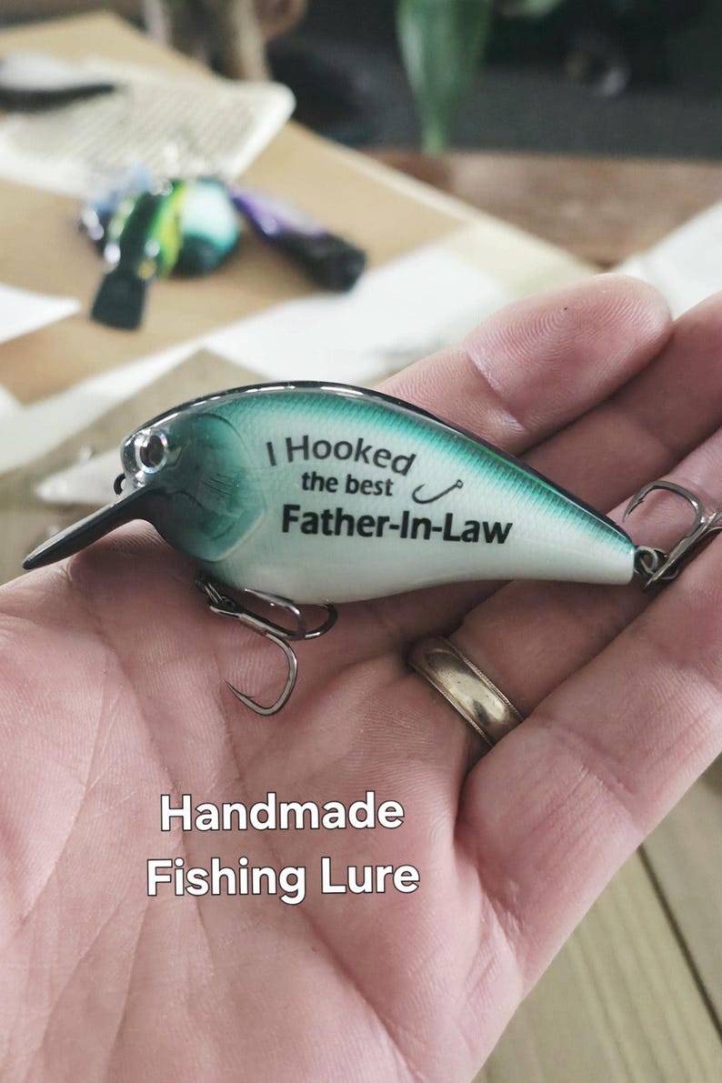 A hand holding a handmade fishing lure with the text "I Hooked the best Father-in-Law" printed on it.