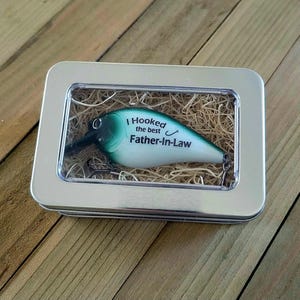 A small fishing lures box with a fishing lures design inside, placed on a wooden surface.