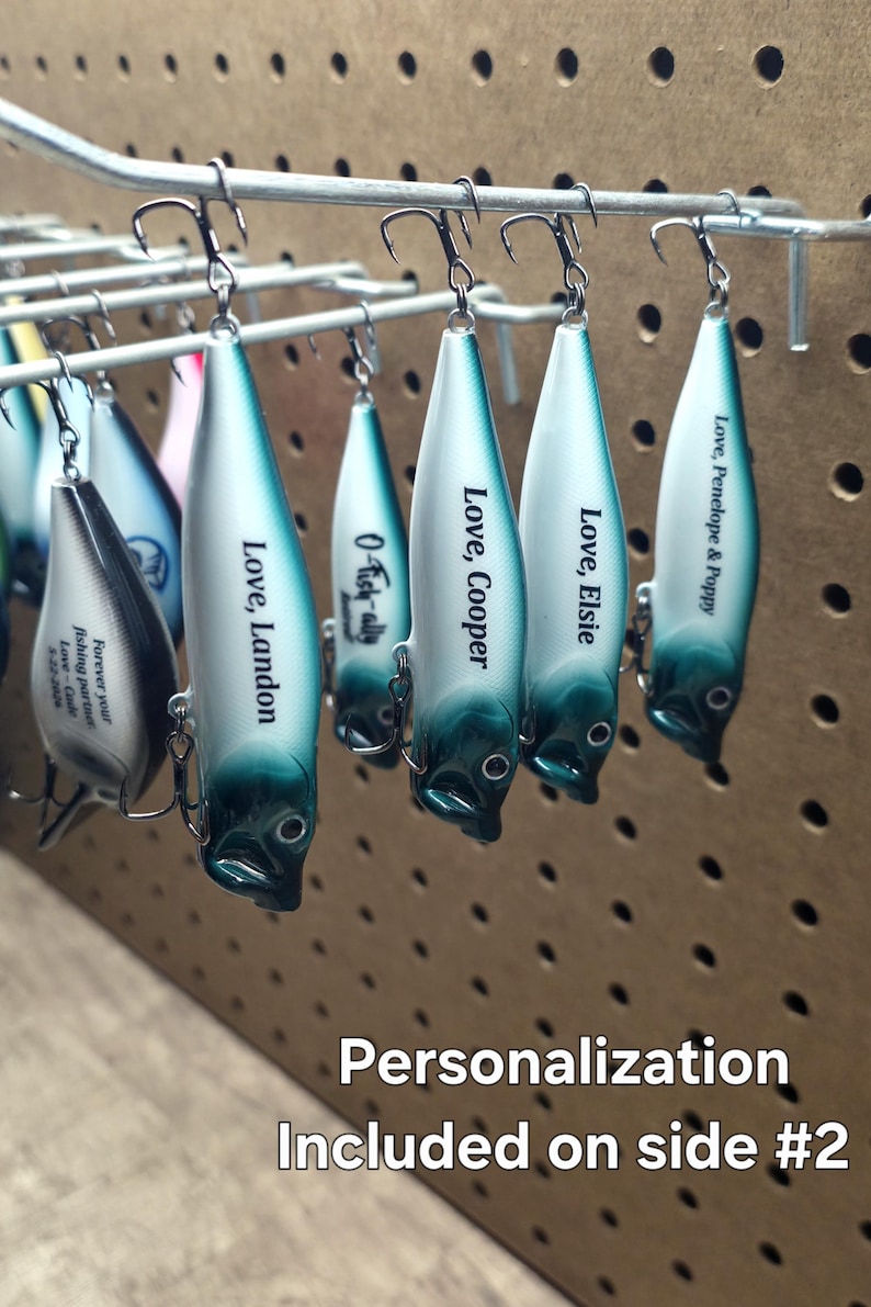 May include: A collection of fishing lures with a white and teal gradient finish, each featuring a metal hook and personalized text including names like Landon, Cooper, Elsie, and Penelope & Poppy, with the text Personalization Included on side #2.