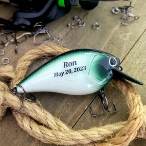 A personalized fishing lures with the name "Ron" and the date "May 20, 2023" printed on it, along with a green and white color scheme.