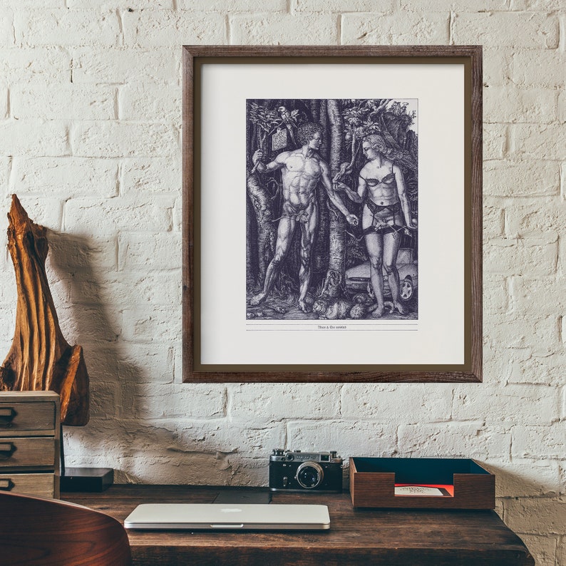 Op de afbeelding: Een zwart-witdruk van een man en een vrouw die in een bos staan. De man houdt een tak in zijn rechterhand en de vrouw houdt een tak in haar linkerhand. De print is ingelijst in een bruin houten lijst.