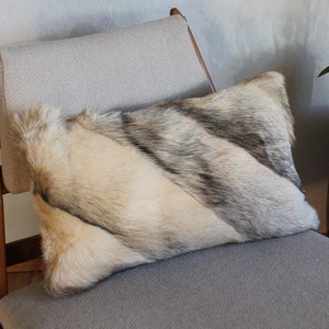 Puede incluir: Un sillón de madera con un cojín de tela gris y una almohada de piel sintética. La silla está junto a una mesa auxiliar negra con un pequeño marco de madera con el número "20" en él.