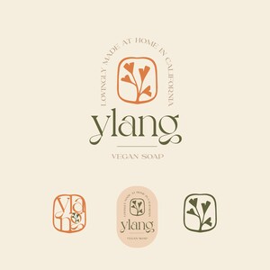 May include: A logo for a vegan soap company called "ylang". The logo features a stylised orange flower with green leaves inside a square. The text "Lovingly Made at Home in California" is written in a circle around the square. The text "ylang" is written in a script font below the square. The text "Vegan Soap" is written in a smaller font below the word "ylang".