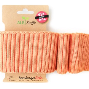 Può includere: Un rotolo di tessuto a costine di colore pesca con un'etichetta che recita "ALB Stoffe", "XXL 140 cm" e "hamburgerliebe by SUSANNE FIRMENICH"