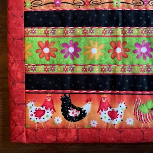 May include: A colorful quilted fabric with a repeating pattern of flowers, chickens, and decorative swirls. The fabric features a red brick-like border and is suitable for various craft projects.