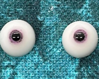 May include: Two spherical doll eyes featuring a smooth white sclera and a detailed iris with a light purple hue surrounding a solid black pupil. The eyes are round and glossy, designed for use in crafting or doll making projects.