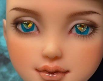 May include: Close-up of a doll face with blue eyes and heart-shaped gems. The doll has light skin, brown eyebrows, and subtle makeup. The lips are a glossy nude color, and the overall aesthetic is delicate and detailed.
