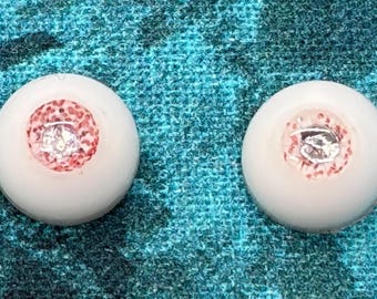 May include: Two spherical doll eyes with smooth white sclera and detailed irises. The irises feature a complex pattern of red and white speckles surrounding a central, reflective silver pupil that mimics the appearance of a realistic human eye.