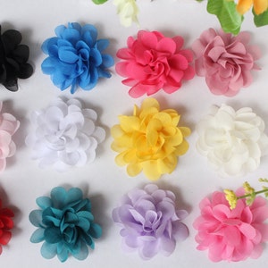 May include: A collection of twelve fabric flower embellishments arranged in a grid. The flowers feature layered, semi-sheer petals in various colors including black, blue, hot pink, dusty rose, light pink, white, yellow, red, teal, and lavender.