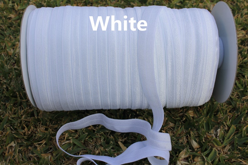 May include: A spool of white elastic ribbon, with the word "White" printed on the spool.