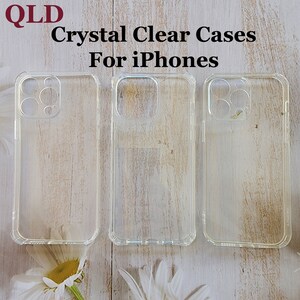 May include: Three clear plastic phone cases for iPhones. The cases are on a light wood surface with white flowers.