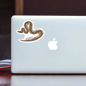 Pu&ograve; includere: Un adesivo con un serpente marrone e bianco con la parola "BAMBOO" stampata sotto. L'adesivo &egrave; su un laptop bianco.