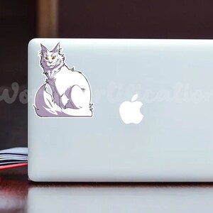 May include: A white cat with yellow eyes sits on a laptop computer. The cat has a fluffy tail and is looking directly at the camera.