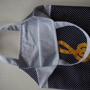 May include: A blue and white polka dot tote bag with a yellow treble clef design. The bag has a white gingham lining and a white handle.