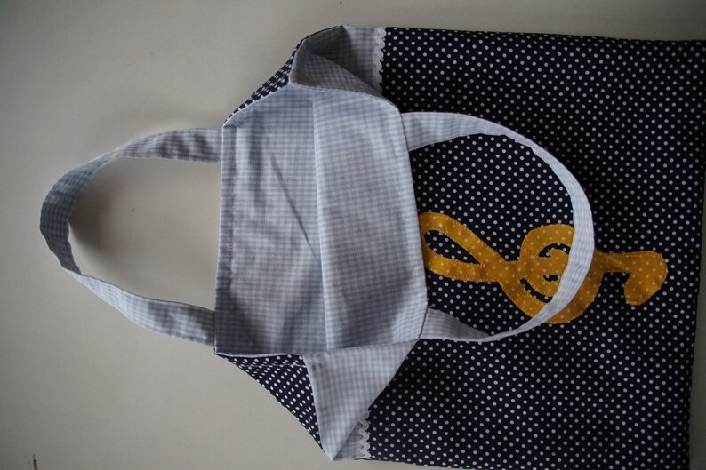 May include: A blue and white polka dot tote bag with a yellow treble clef design. The bag has a white gingham lining and a white handle.