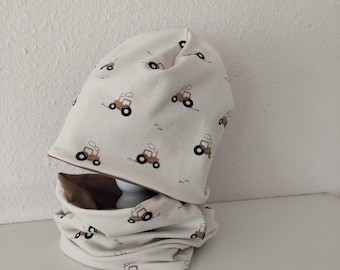 May include: A cream-colored beanie hat and a matching neck warmer set. Both items feature a repeating pattern of small brown tractors with black wheels and white smoke puffs. The neck warmer has a solid brown interior lining visible at the top.