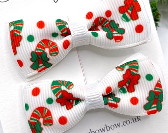May include: Two white bow hair clips with a Christmas candy cane pattern. The bows have red, green, and white designs. The card behind the bows has the text "Honeybowbow accessories" and "www.honeybowbow.co.uk".