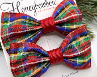 May include: Two red, green, blue, and white plaid hair bows with red centers. The bows are on a white card with the text "Honeybowbow accessories" and a website address.