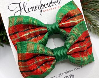 May include: Two green, red, and gold plaid hair bows with green centers. The bows are attached to a white card with the text "Honeybowbow accessories" and a website address.