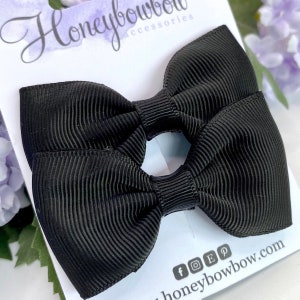 Puede incluir: Dos lazos para el pelo negros con textura acanalada. Los lazos se muestran en una tarjeta blanca con el texto "Honeybowbow accessories" en una fuente cursiva. Se ven iconos de redes sociales y una dirección web.