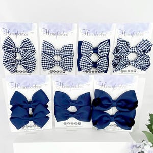 May include: A collection of hair bows in various styles and colors. The bows include gingham patterns in black and white, and solid navy blue bows. Each bow is attached to a card with the text "Honeybowbow".