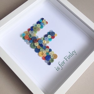 May include: A white frame with a white background and a letter F made out of colourful buttons. The text "F is for Finley" is written in green below the letter.