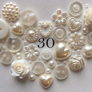 May include: A heart-shaped arrangement of white buttons, pearls, and decorative flowers. The number 30 is in the center of the arrangement.