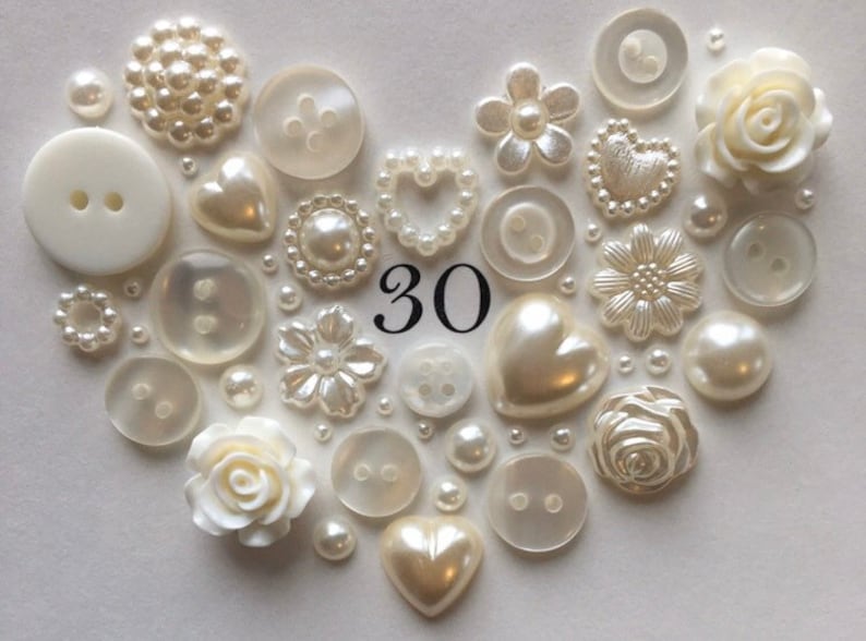 May include: A heart-shaped arrangement of white buttons, pearls, and decorative flowers. The number 30 is in the center of the arrangement.