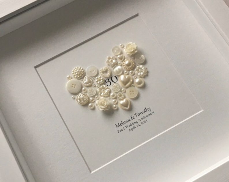 May include: A white framed picture with a heart made of white buttons and pearls. The number 30 is in the center of the heart. The text below the heart reads "Melissa & Timothy Pearl Wedding Anniversary April 18, 2021."