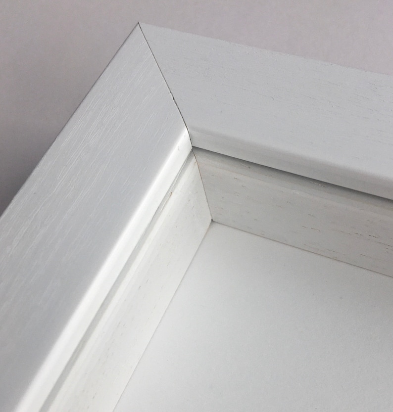 May include: Close-up of a white picture frame with a simple, clean design. The frame is made of wood and has a smooth finish.