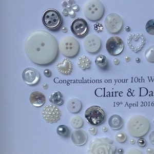 May include: A white card with a silver and white button design. The card says "Congratulations on your 10th Wedding Anniversary Claire & Dave 19th April 2016".