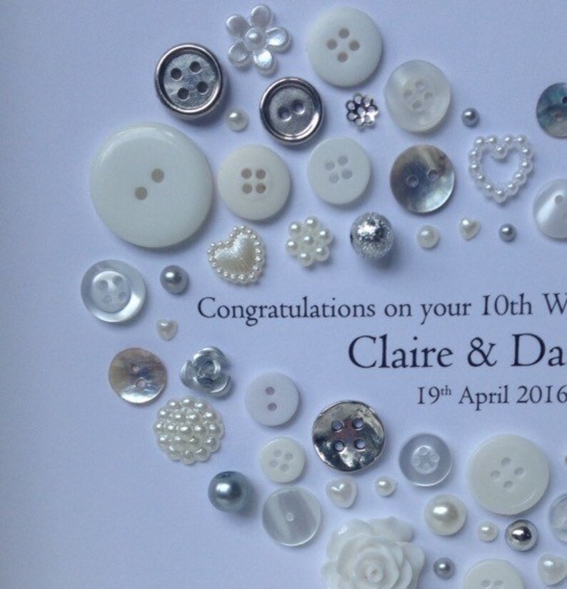 May include: A white card with a silver and white button design. The card says "Congratulations on your 10th Wedding Anniversary Claire & Dave 19th April 2016".