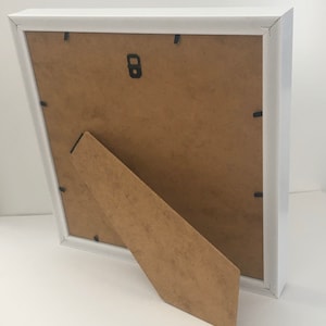 May include: White picture frame with a brown cardboard backing and a fold-out easel stand.