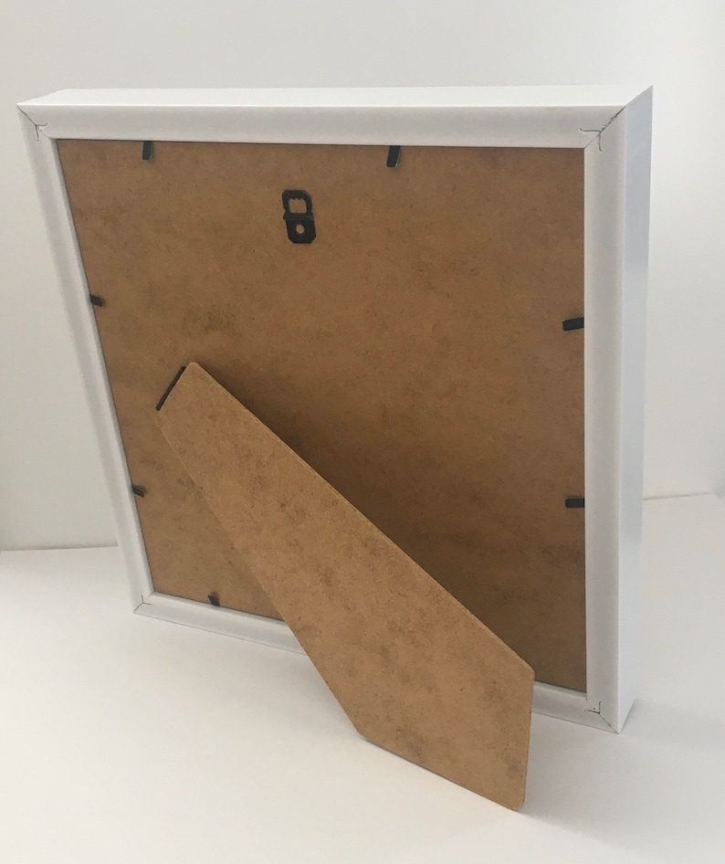 May include: White picture frame with a brown cardboard backing and a fold-out easel stand.