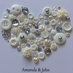 May include: A white heart-shaped arrangement of buttons, pearls, and other embellishments. The heart is surrounded by a white background and the text "Amanda & John" is written below the heart.