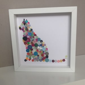 May include: A framed artwork featuring a cat silhouette made from colorful buttons. The cat is sitting with its tail curled behind it. The buttons are various sizes and colors, including red, blue, green, yellow, and purple.