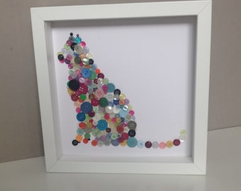 May include: A framed artwork featuring a cat silhouette made from colorful buttons. The cat is sitting with its tail curled behind it. The buttons are various sizes and colors, including red, blue, green, yellow, and purple.