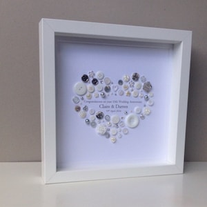 May include: A white framed picture with a white background and a heart made of white and silver buttons. The text "Congratulations on your 10th Wedding Anniversary Claire & Darren 19th April 2016" is written below the heart.