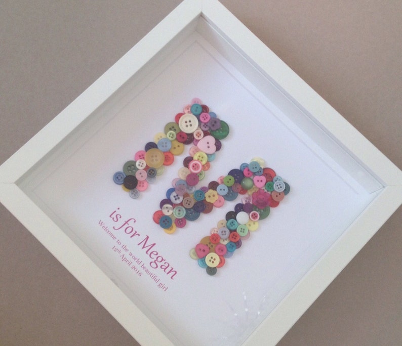 May include: A white frame with a white background and a letter M made of colorful buttons. The text "is for Megan" is written below the letter M. The text "Welcome to the world beautiful girl 12th April 2015" is written below the text "is for Megan".