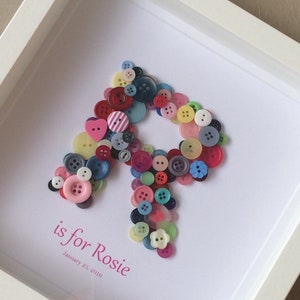 May include: A framed artwork featuring the letter "R" made from colorful buttons. The text "R is for Rosie" and "January 25, 2016" is written below the letter.