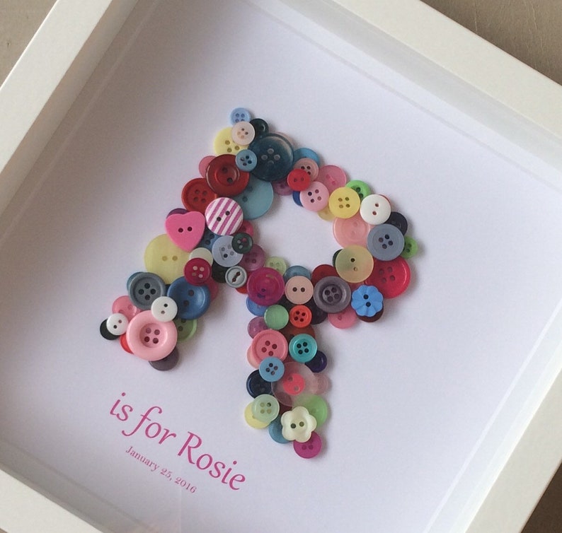 May include: A framed artwork featuring the letter "R" made from colorful buttons. The text "R is for Rosie" and "January 25, 2016" is written below the letter.