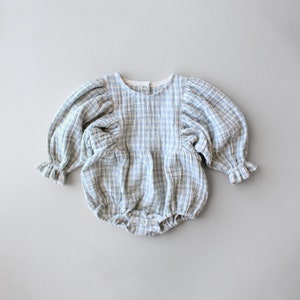 May include: A blue and white gingham baby onesie with puffed sleeves and a ruffled trim. The onesie has a round neckline and snaps at the crotch.
