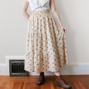 Puede incluir: Una falda larga de vuelo con estampado floral en tonos rojos y crema. La falda tiene una cintura elástica y una silueta fluida.