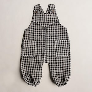 May include: Black and white gingham baby overalls with two front pockets and adjustable straps. The overalls have a button closure on the straps and at the waist. The fabric is a lightweight cotton, perfect for warm weather.