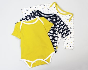 May include: Three baby onesies in different patterns. One is yellow with white trim, one is black and white geometric, and one is white with a small animal print.