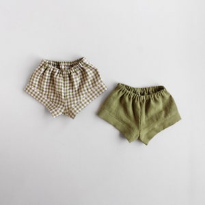 Puede incluir: Dos pares de pantalones cortos de lino. Un par es verde y el otro es verde y blanco a cuadros.