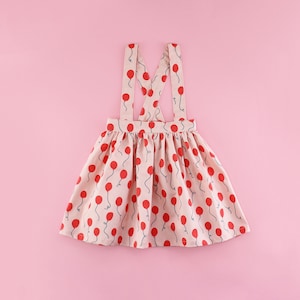 May include: A pink and red patterned overall skirt with thin straps. The skirt has a red balloon print.